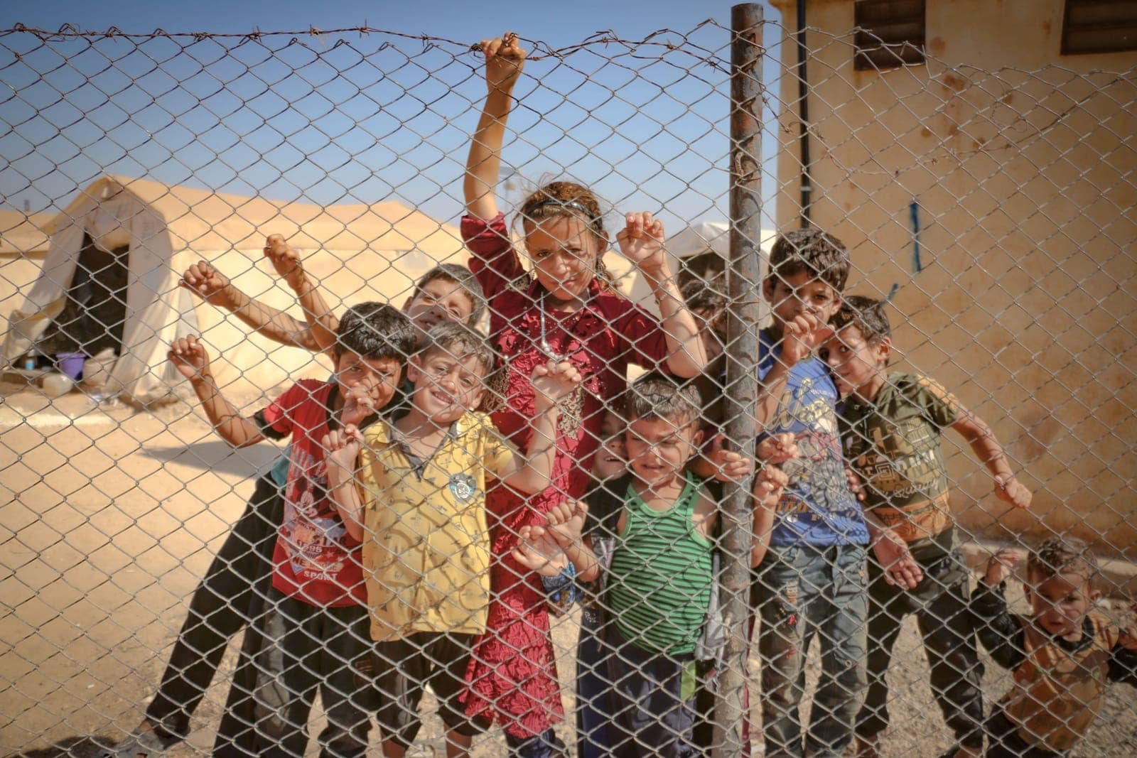 A group of children holding onto a chain-link fence at a camp